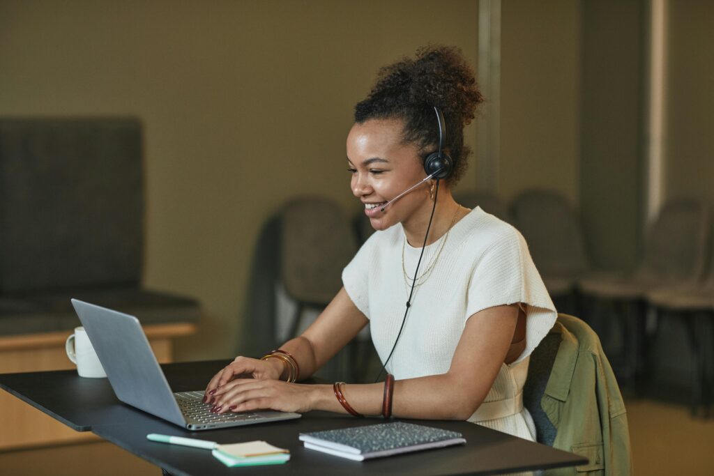 African American woman in a call center setting, working on a laptop and wearing a headset.